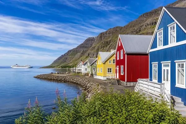 Row of brightly coloured houses along a coastal fjord in Iceland with a cruise ship in the distance